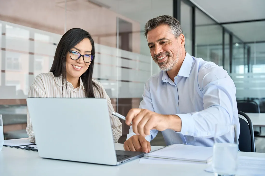 Two colleagues smiling while reviewing work together on a laptop